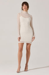 A woman is wearing a white dress with a fitted silhouette. The dress has a high neckline and features a sleeveless design with long, sheer lace sleeves. The lace material has a floral pattern, and the dress combines a lace overlay with a solid lining underneath. She pairs the dress with open-toed high heels.